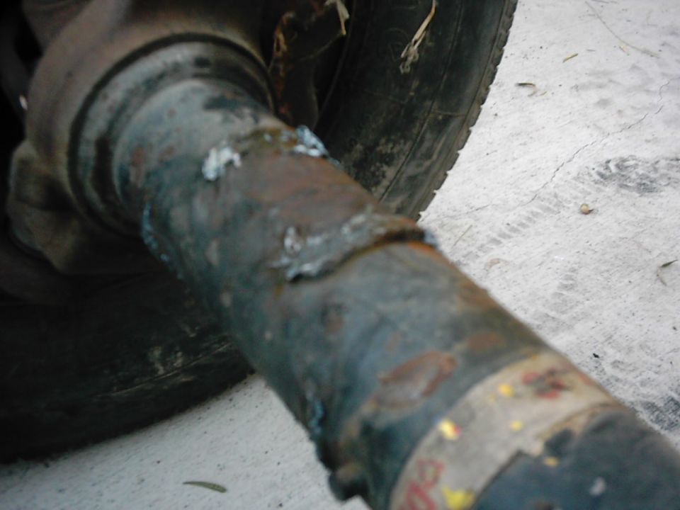 Rusty axle tube with welds and a tire. Supermotors.net logo visible