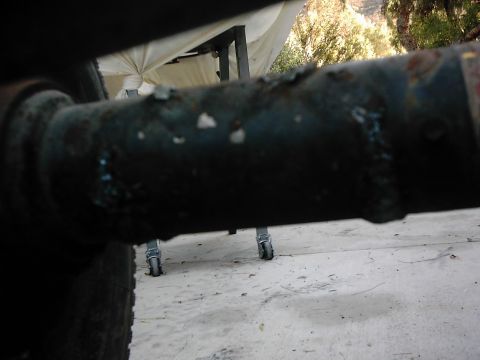1978 Ford Bronco - Close-up of a rusted metal pipe, with a white tarp and wheels in the background.