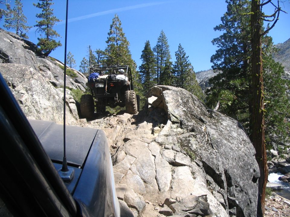 Off-road rig crawling up a slab of granite on a high mountain trail with a whip antenna