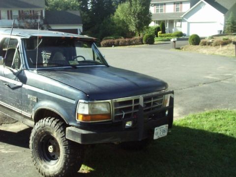 1992 Ford Bronco - A dark blue 1992 Ford Bronco is parked in a suburban driveway, showing its front three-quarter view.