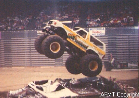 1993 Ford Bronco - Monster truck performs a jump in an arena with spectators in the background.