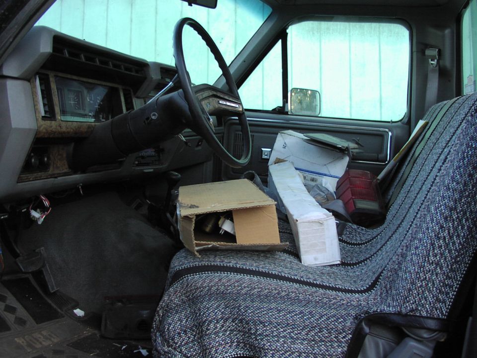 Interior of a truck cab with a steering wheel, dashboard, and a seat covered in boxes