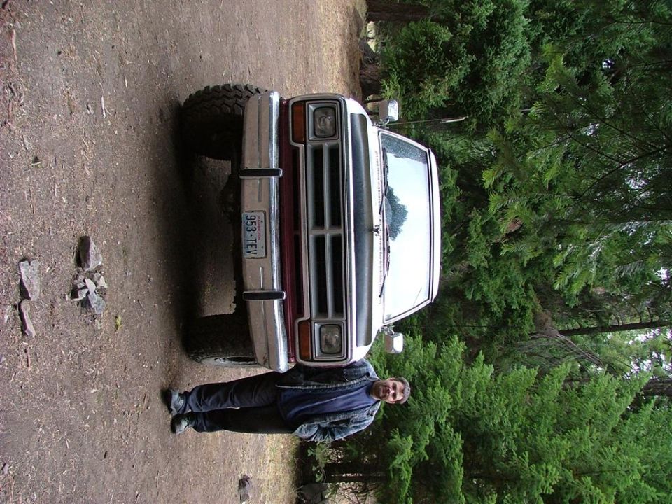 Two-tone maroon and silver pickup on dirt forest road with man standing beside it