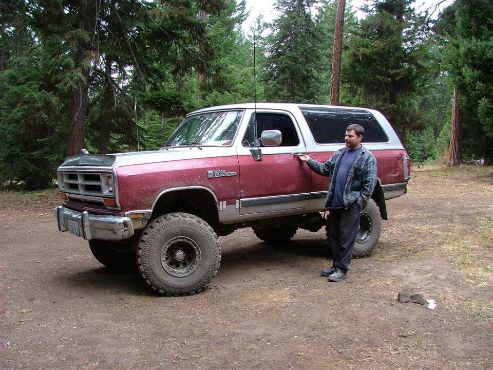 Lifted maroon and white Dodge Ramcharger 4x4 in a forest clearing with a person standing beside it