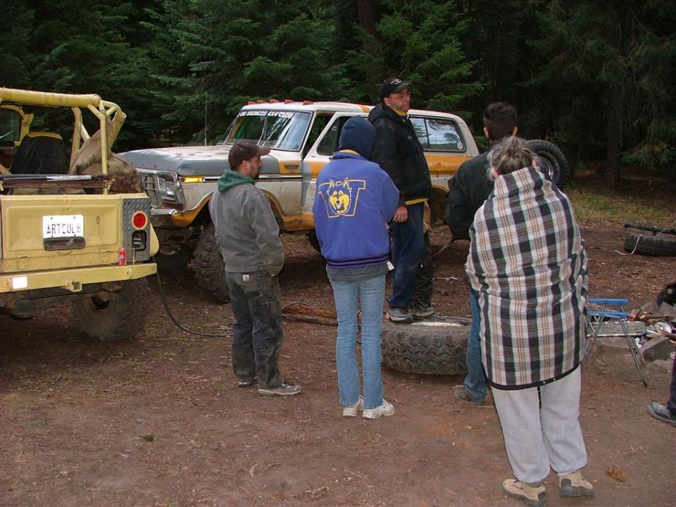 People around a lifted white and tan Ford Bronco at a wooded 4x4 club trail camp