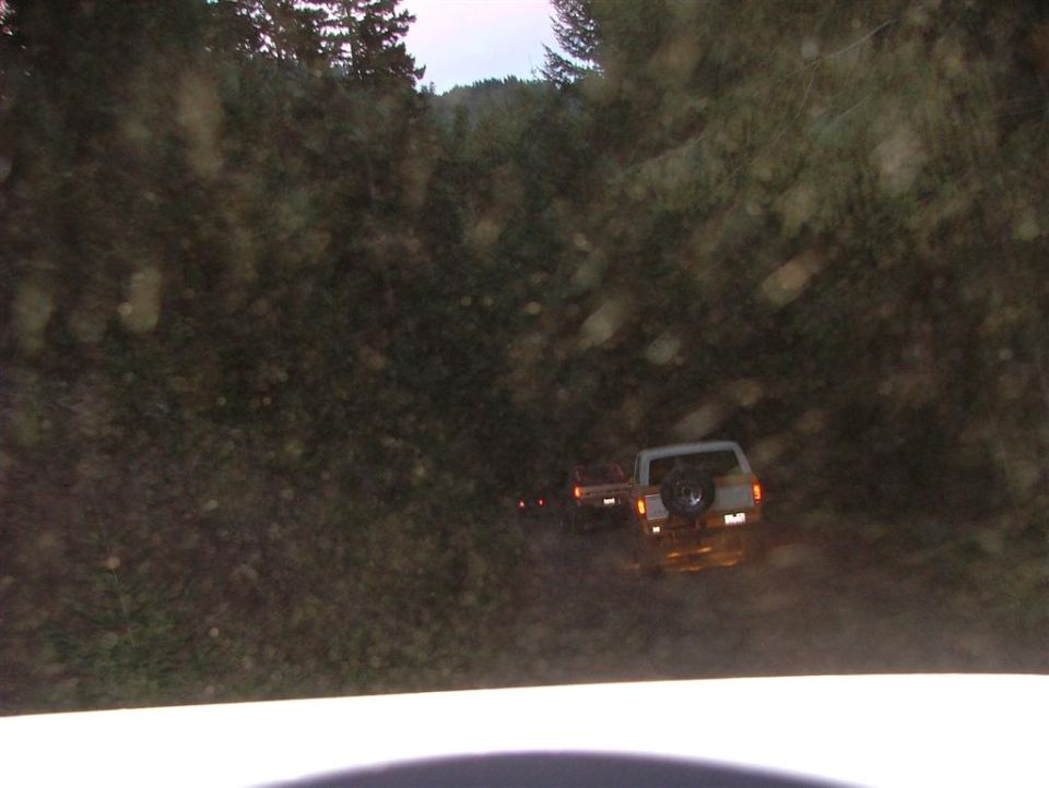 Rear view of white pickup truck with spare tire on back, driving on dirt road
