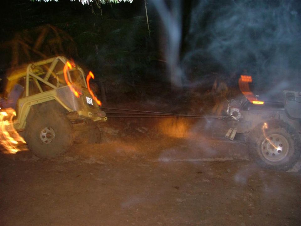 Night winch recovery, yellow caged Jeep pulled by cable from a dark 4x4 in smoke and dust