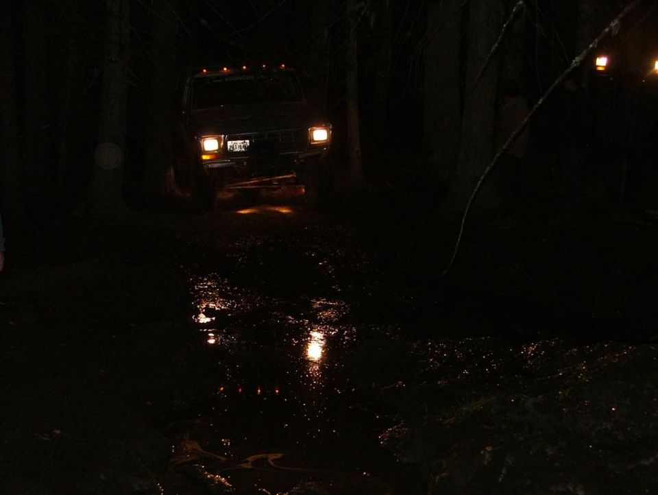 Dark 1989 Dodge Power Ram driving through muddy woods at night, headlights on