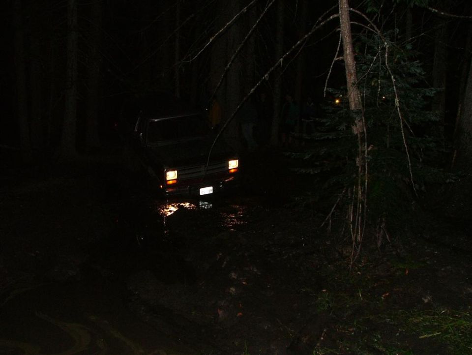Dark 4x4 truck with headlights on nosed into a muddy water hole at night