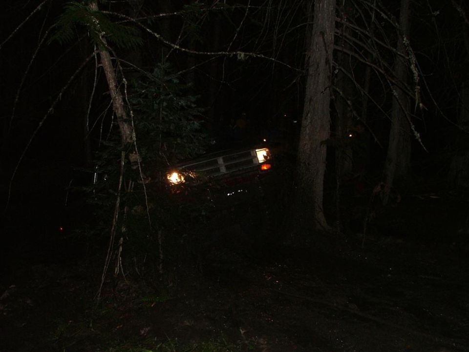 4x4 leaning at a steep angle in dark woods at night, headlight and grille visible