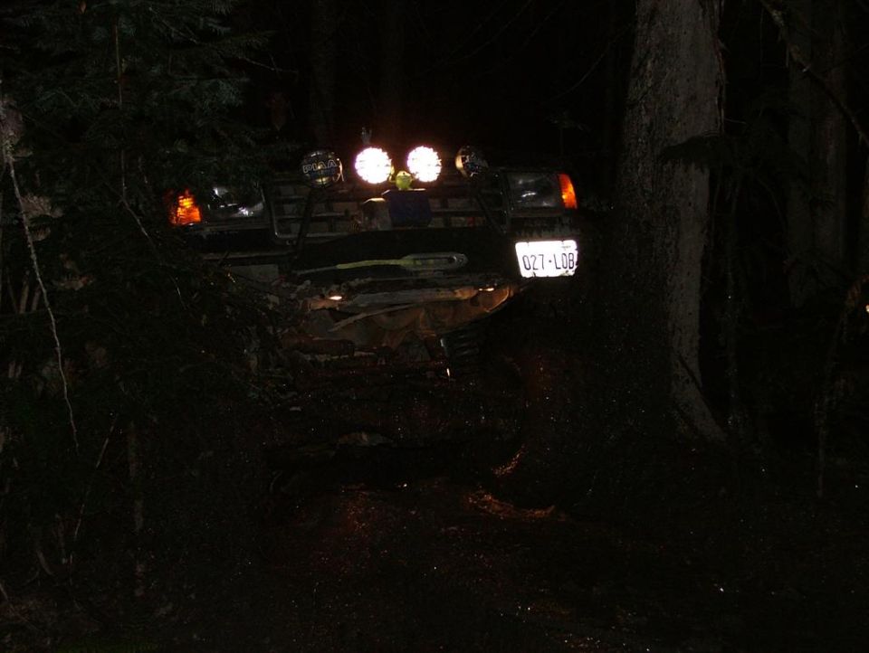 Off-road vehicle with auxiliary lights on, license plate 027-L08, at night in a wooded area