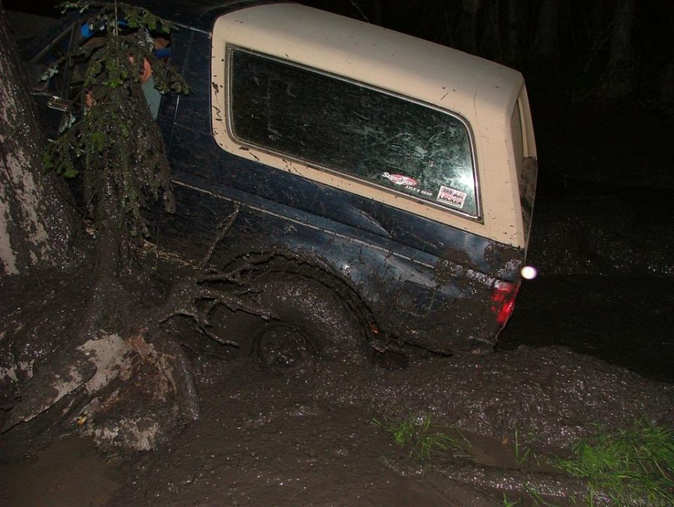 Truck stuck deep in mud next to a tree, with a camper shell on the back