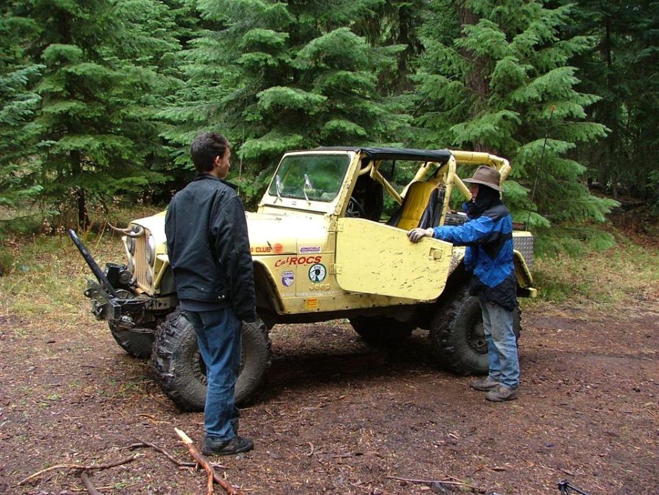 Yellow off-road vehicle with roll cage and large tires. Two people stand near it
