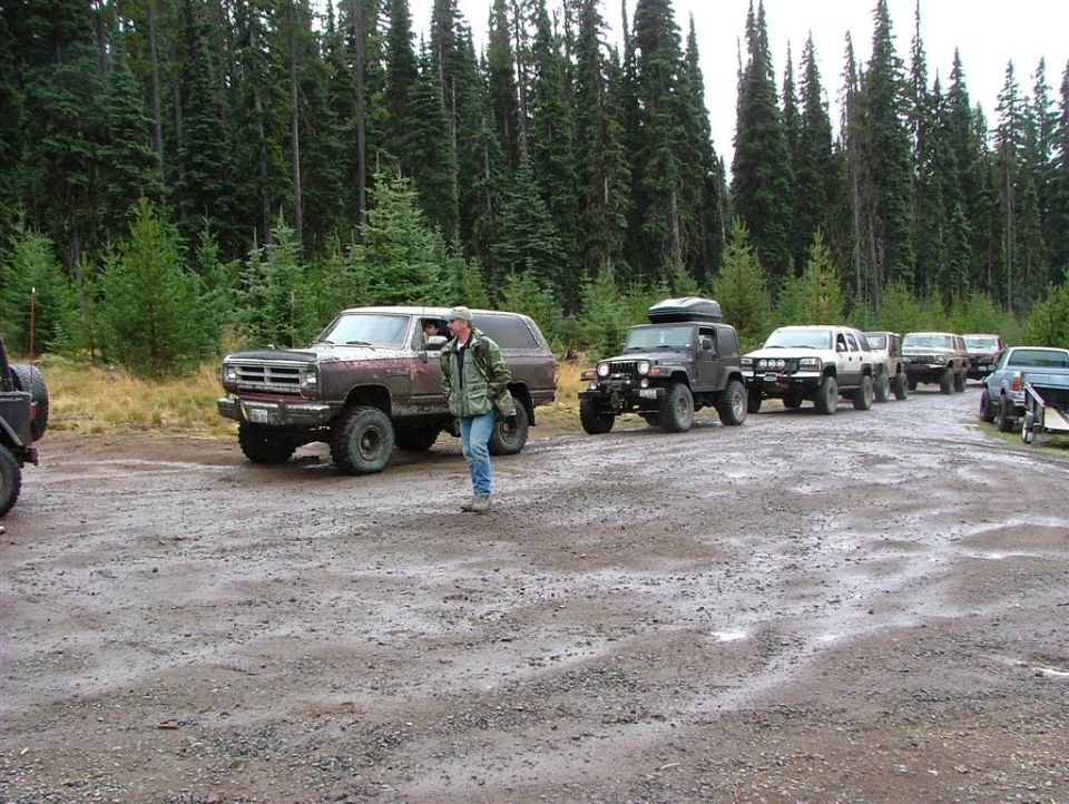 Muddy burgundy Dodge Ramcharger leading a line of 4x4s in a gravel staging lot