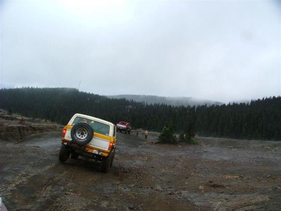 Lifted white and orange SUV with tailgate spare tire climbing a wet gravel bank