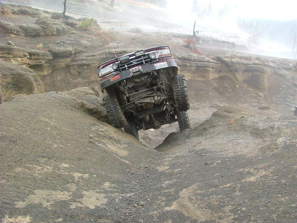Maroon off-road vehicle tilted on rocky terrain, front grille visible with aftermarket lights