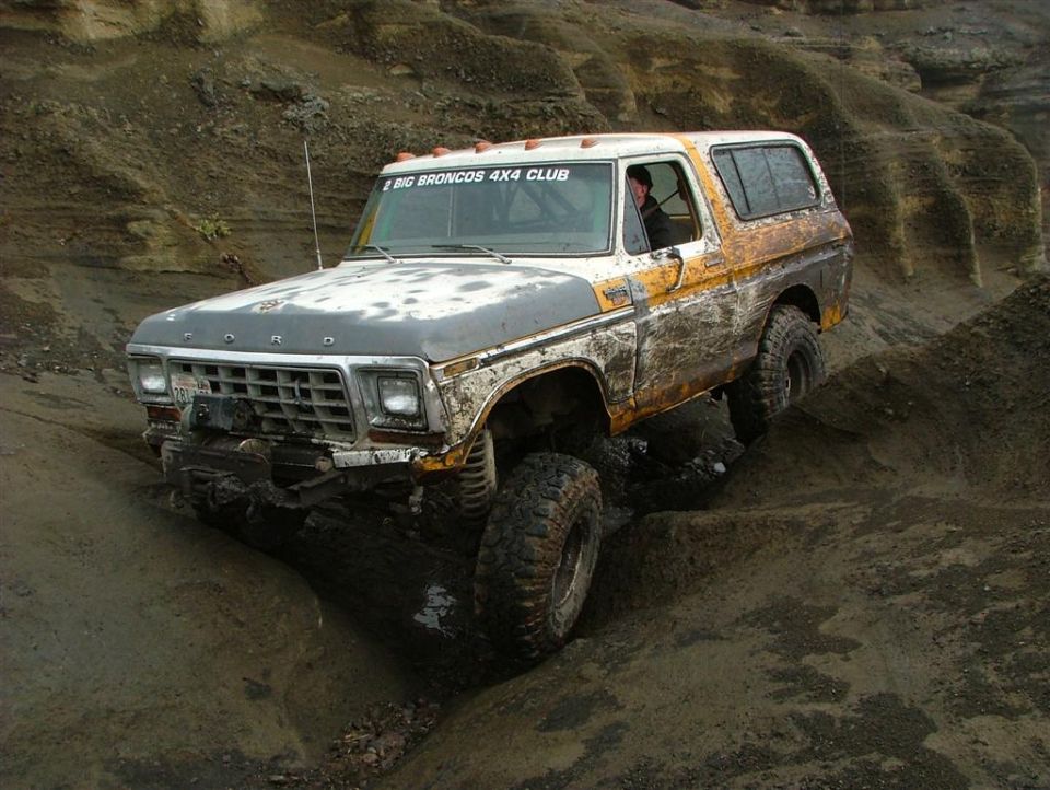Ford Bronco climbing muddy terrain, "BIG BRONCOS 4X4 CLUB" sticker on door