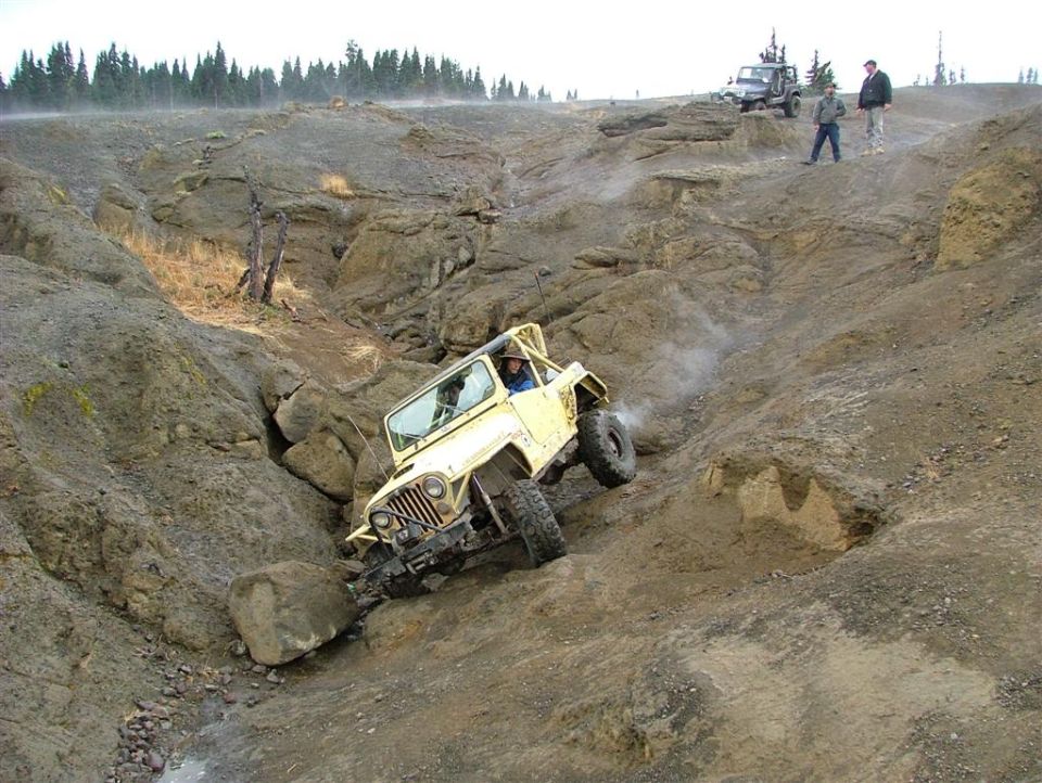 yellow jeep going down a rocky hill, another jeep and two people on top