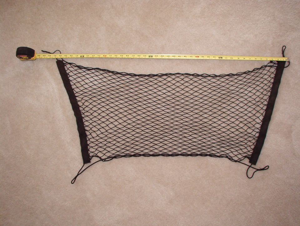 Black mesh cargo net laid on carpet next to a tape measure showing its width