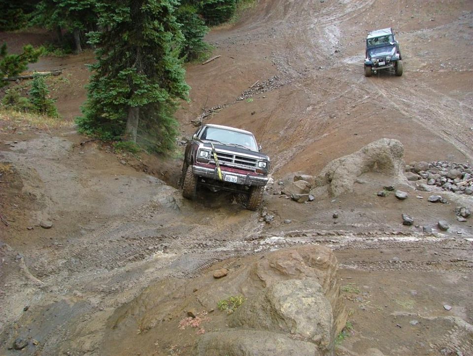 1989 Dodge Power Ram navigating a steep, muddy off-road path with another Jeep in the background