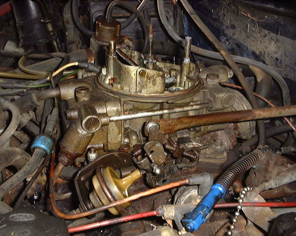 Dirty, rusty carburetor on engine of 1987 Ford Bronco with hoses and linkage visible