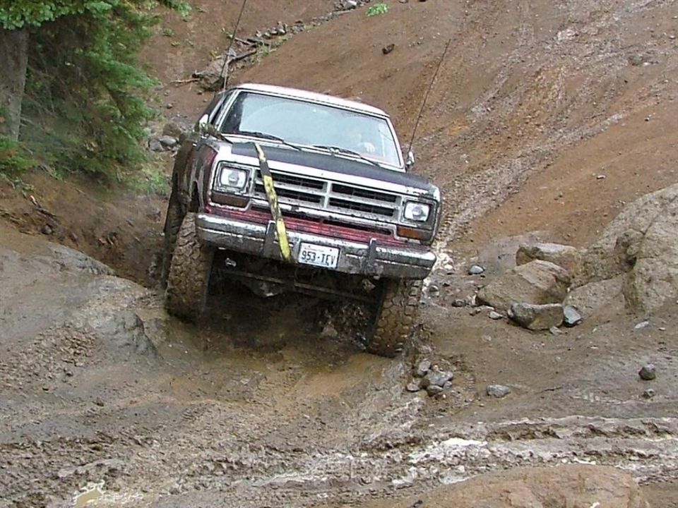 Maroon and white Dodge pickup climbing a muddy, rutted off-road trail