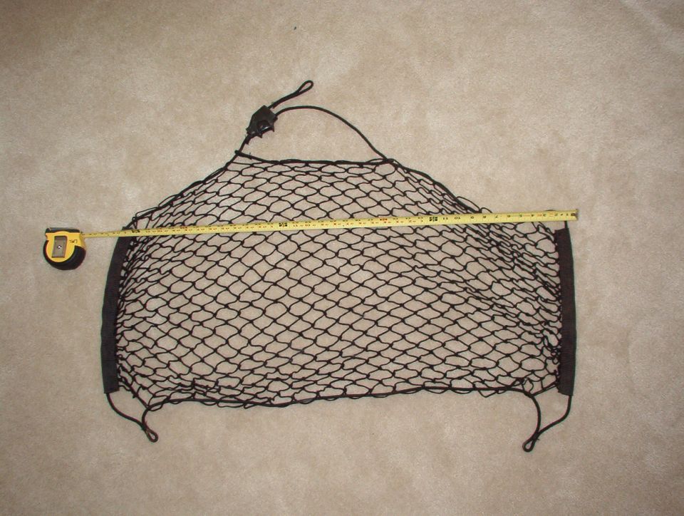 Black elastic cargo net on tan carpet with a tape measure spanning its width