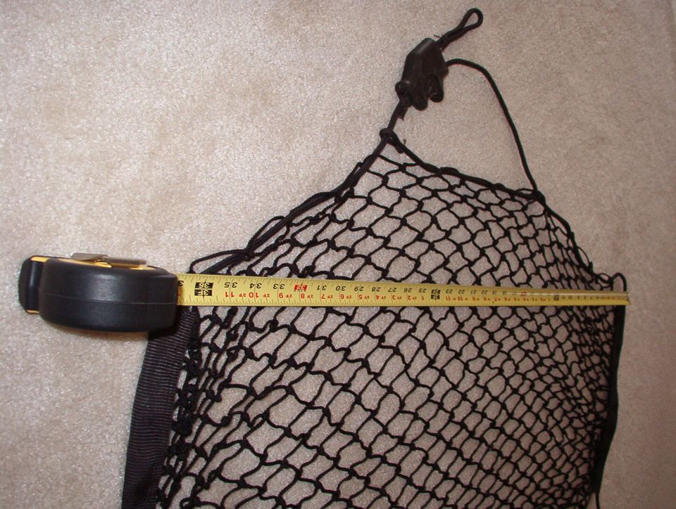 Black cargo net on carpet measured for height with a tape measure across the middle
