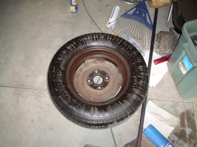 Rusty steel wheel with mounted tire lying flat on a garage floor near tools