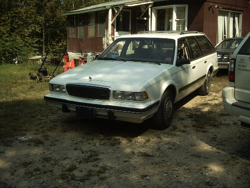 White station wagon parked in front of a house, with another vehicle to the right