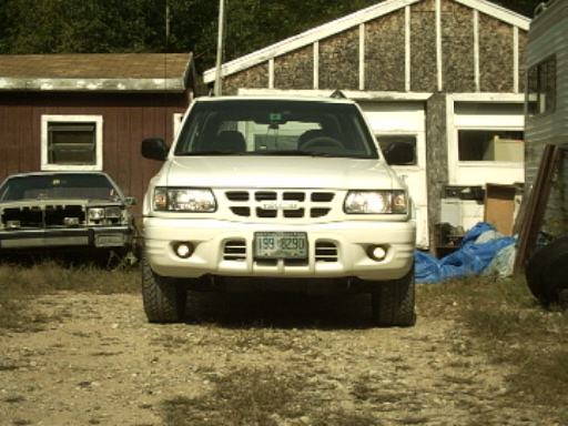 Front view of a white SUV parked in front of a garage. Another car is to the left