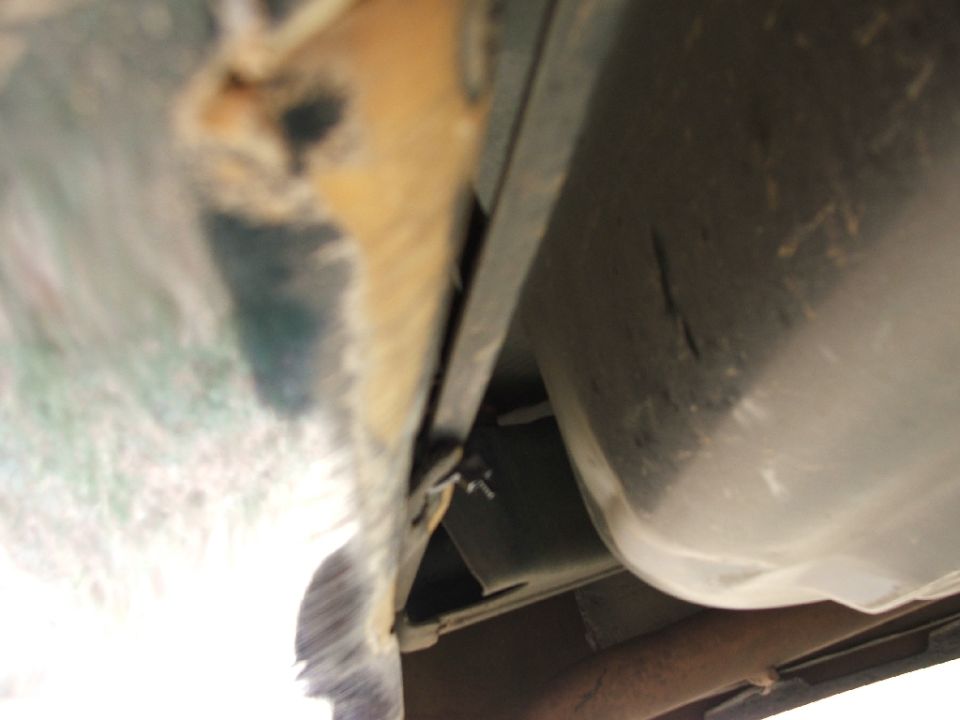 Blurry view under a vehicle showing rusty rocker panel edge and plastic fuel tank