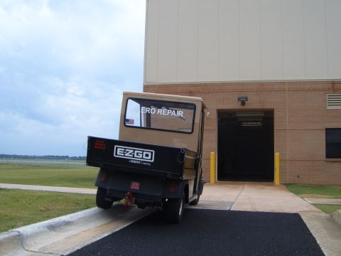 1988 Ford Bronco - An EZGO utility vehicle with 'ERO REPAIR' on the rear window drives up a ramp towards a building entrance.