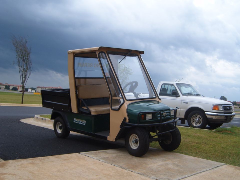 Green and tan utility vehicle parked next to white pickup truck