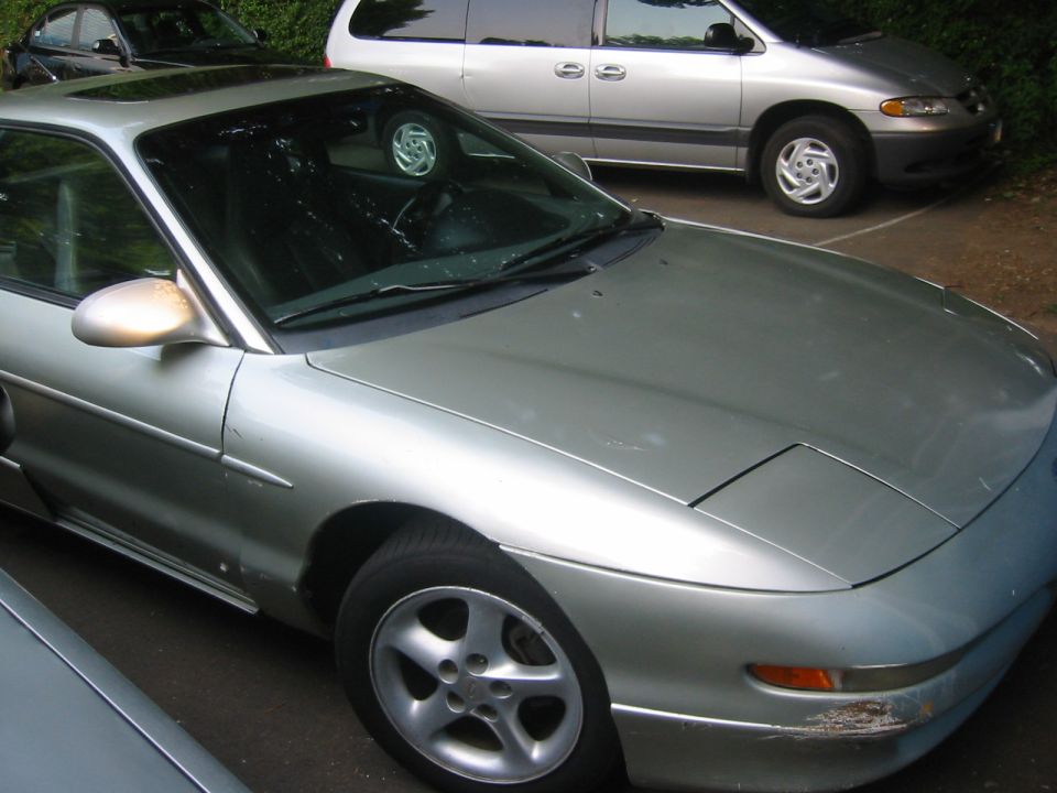 Silver Ford Probe coupe parked in gravel lot beside a silver minivan, front three-quarter view