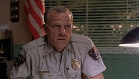 1995 Ford Bronco - A man in a police-like uniform sits at a desk, looking off to the side.