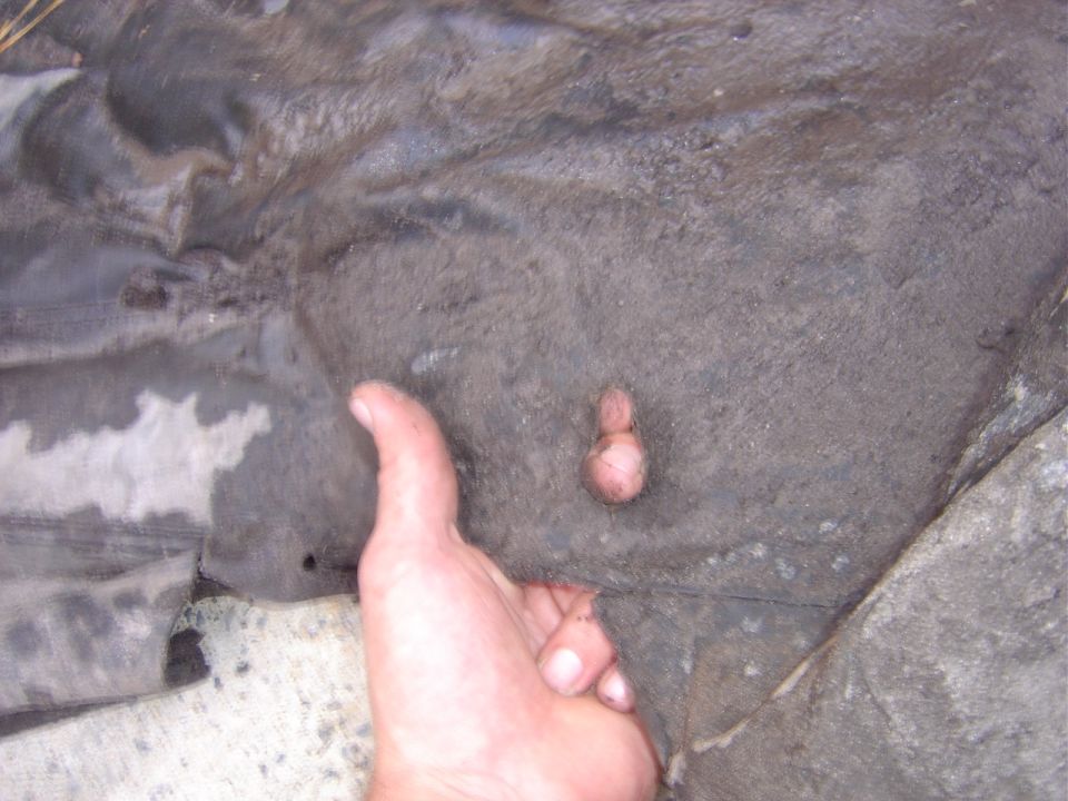 Close-up of a dirty vehicle undercarriage part with a human hand for scale