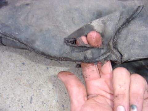 1987 Suzuki Samurai - A hand points to a torn section of a rubber automotive part, likely a mud flap or undercarriage shield.
