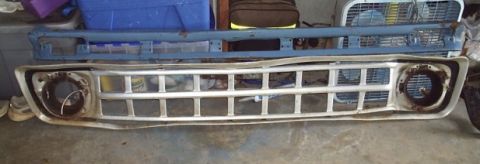 1989 Ford Bronco - Two vehicle grilles are displayed on a concrete surface, with various items in the background.