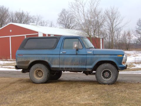 1979 Ford Bronco - A blue 1979 Ford Bronco is parked on a dirt road in front of a red barn.