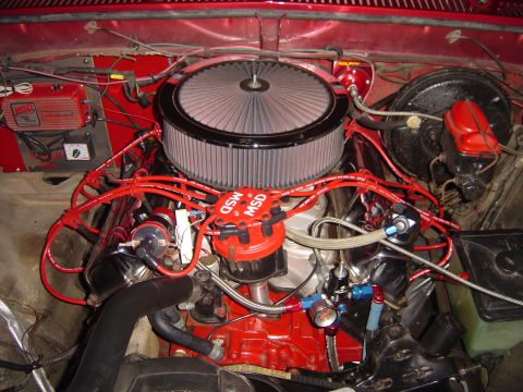 1978 Ford Bronco - Overhead view of a red V8 engine bay with a chrome-lipped round air cleaner over the carburetor, red MSD distributor cap and red MSD plug w…