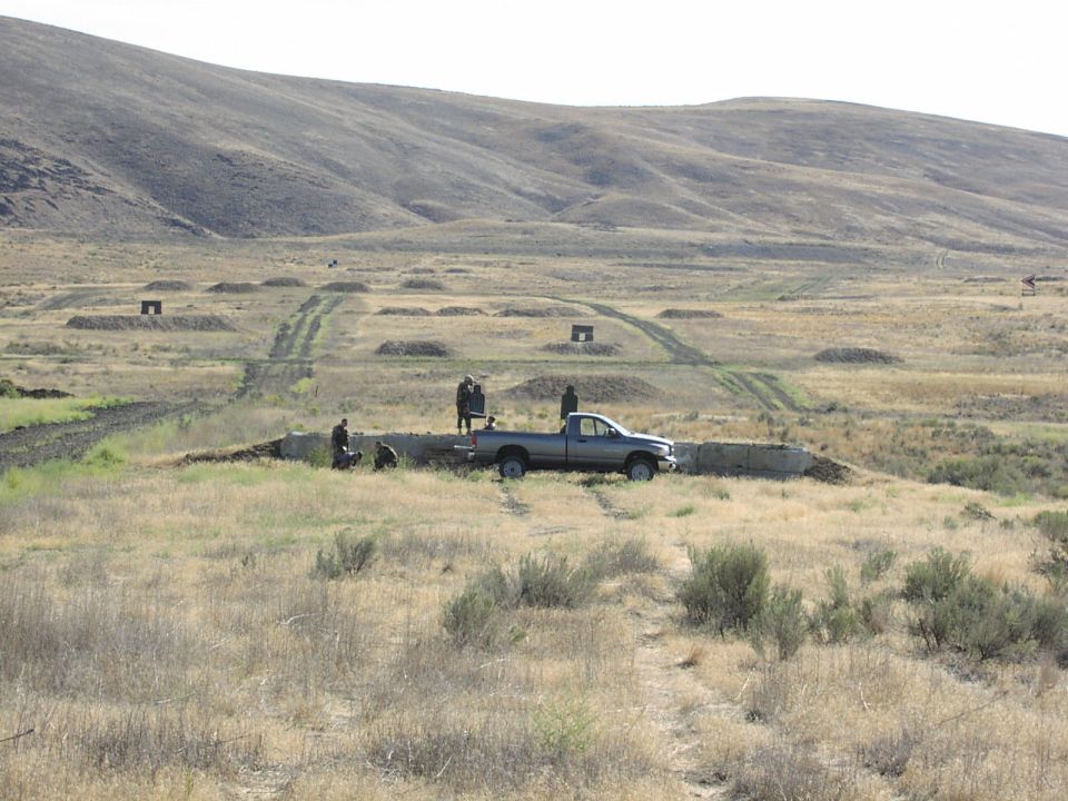 gray pickup truck parked on a berm with people around it at a shooting range