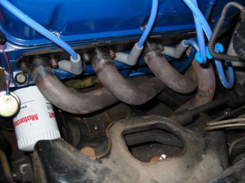 1985 Ford Crown Victoria LTD - Close-up view of an engine's exhaust manifold and spark plug wires, with a visible oil filter.