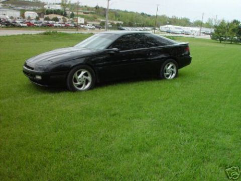 1992 Ford Probe - A black 1992 Ford Probe is parked on a grassy lawn with a distant view of buildings and cars.