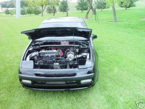 1992 Ford Probe - The engine bay of a black car is visible with the hood raised, parked outdoors on a grassy lawn.