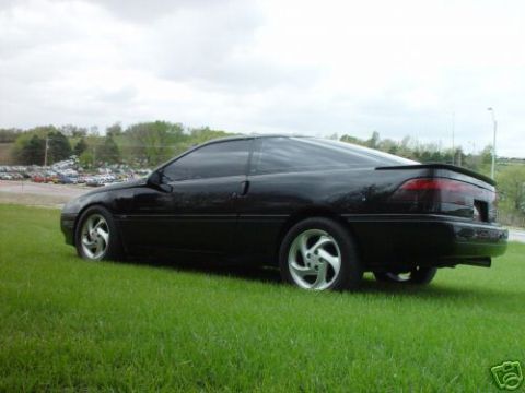 1992 Ford Probe - A black 1992 Ford Probe is shown from the rear quarter angle, parked on a grassy area with a parking lot in the distance.