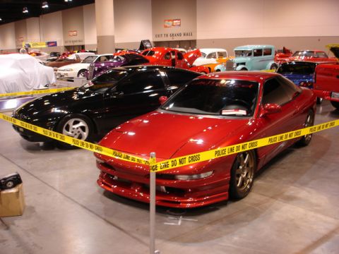1992 Ford Probe - A red sports car is displayed behind police line tape at an indoor event.