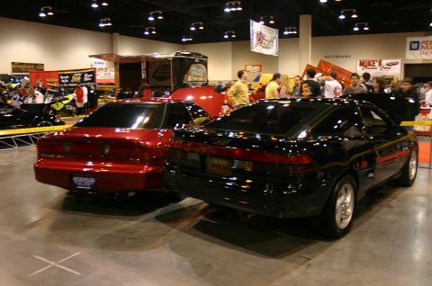 1992 Ford Probe - Two sporty coupes are displayed indoors at what appears to be a car show or exhibition.