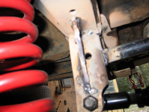 1995 Ford Bronco - Close-up view of vehicle suspension and frame modifications, including a red coil spring and welded metal parts.