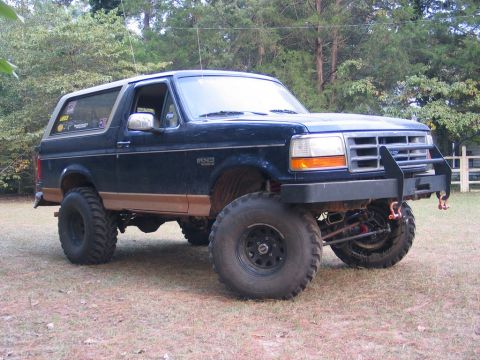 1995 Ford Bronco - This lifted Ford Bronco sits on a grassy area with trees in the background.